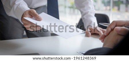 Employee handed over a document envelope and a box of work equipment beside him, Businessman submits resignation documents to their supervisor and take personal equipment in a brown box. Royalty-Free Stock Photo #1961248369