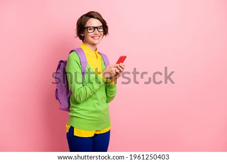 Photo of cute young lady dressed yellow shirt glasses backpack holding modern device empty space isolated pink color background