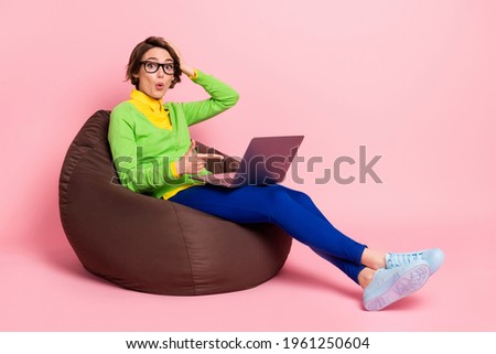 Profile side photo of impressed lady dressed yellow shirt glasses sitting bean bag pointing modern gadget isolated pink color background
