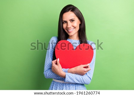 Photo of funny sweet young woman dressed blue outfit embracing red hear smiling isolated green color background