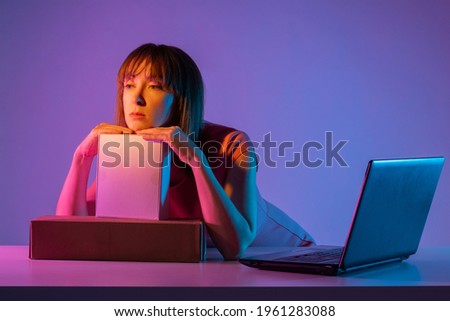 Girl with boxes. Woman with laptop on gray background. Girl employee of an online store. Woman works in an online store. She was thinking about something, dreaming. Online store career.