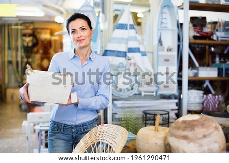 Happy cheerful positive smiling woman standing with wooden box in decoration and furniture store Royalty-Free Stock Photo #1961290471