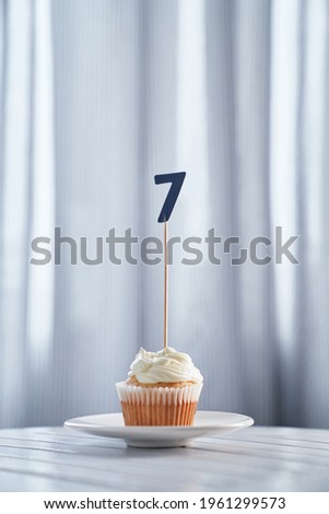Homemade birthday cupcake with creamy topping and number 7 seven on white plate. Minimalistic birthday or anniversary concept. High quality vertical image