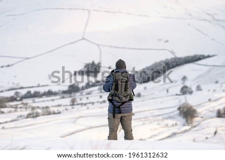 Photographer wrapped up warm in snow covered mountain landscape taking pictures of hillside range with backpack looking at amazing view with trees and deep snowfall from blizzard.