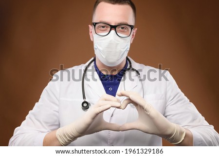 male doctor making heart gesture with fingers, looking at the camera. studio photography