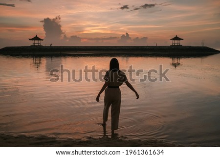 
The girl touches the ocean with her foot and admires the beautiful sunrise on the beach.