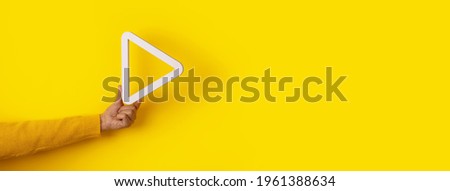 3d media play button in hand over yellow background, panoramic layout