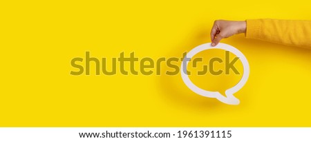 Dialogue bubble in hand over yellow background, panoramic image Royalty-Free Stock Photo #1961391115