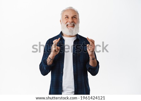Smiling hopeful old man making wish. Senior guy with tattoos looking up with optimistic face while praying, waiting for results, anticipating good news, standing over white background