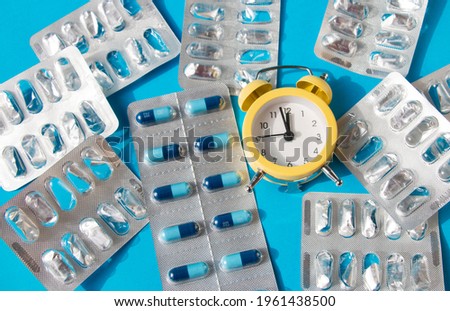 Mountain of empty plates from tablets, one full with blue capsules. Chances alarm clock Taking medicine for treating serious diseases