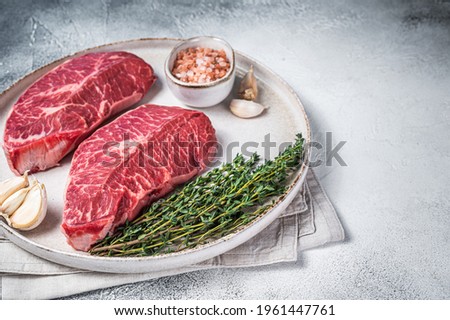 Raw Oyster Top Blade or flat iron roast beef meat steaks on a plate with herbs. White background. Top View. Copy space Royalty-Free Stock Photo #1961447761