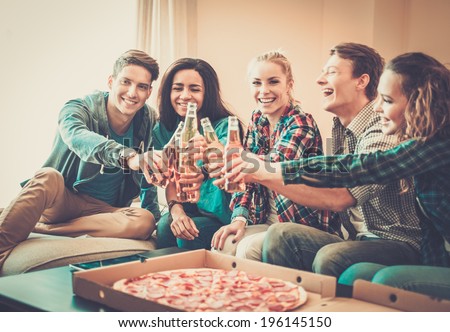 Group of young multi-ethnic friends with pizza and bottles of drink celebrating in home interior