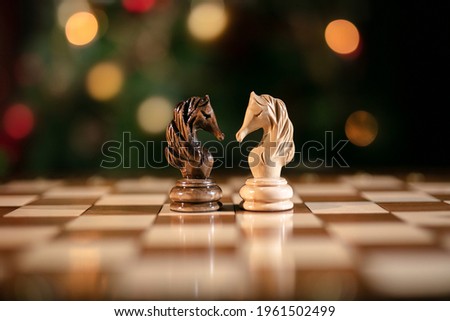Chess pieces on wooden chess board. Christmas or New Year Intellectual gift concept. Checkmate figures on a bokeh lights on Christmas tree 