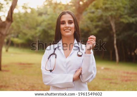 Portrait of young adult female doctor or nurse wearing lab coat and stethoscope outside.