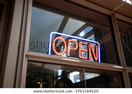 Red and blue lit open neon sign in a retail store or restaurant window on a sunny day.