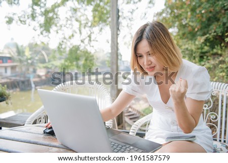 Euphoric asian woman with white dress looking on labtop in an urban park.