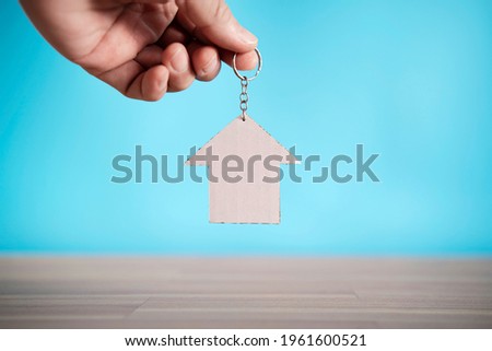 Close-up of hand holding keys and paper house model against blue background