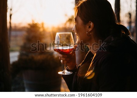 young woman holding a glass of red wine, outdoors, at sunset. Royalty-Free Stock Photo #1961604109