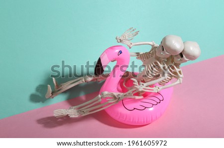 Inflatable flamingo with skeletons on blue-pink background. Minimalism. Trendy shadow. Halloween party. Creative layout.