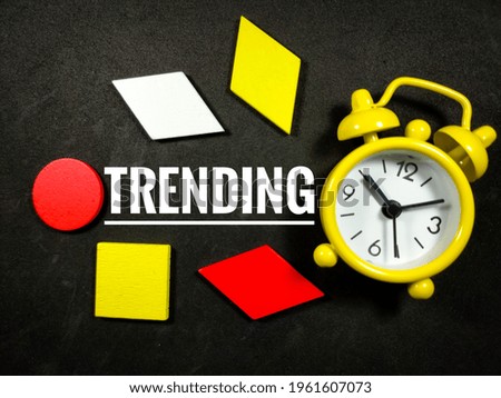 Text TRENDING with colorful wooden jigsaw and alarm clock on black background.