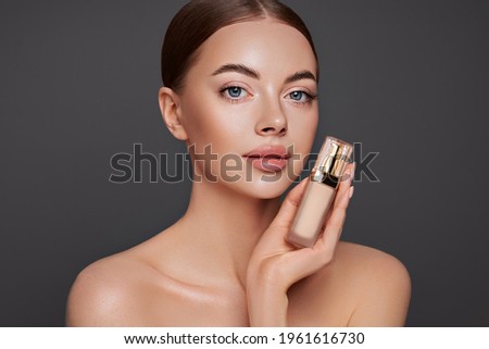 Portrait beautiful young woman with clean fresh skin. Model with foundation makeup bottle. Cosmetology, beauty and spa Royalty-Free Stock Photo #1961616730