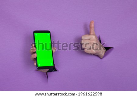phone with green screen in hand on purple background, hand gesture, through the background hand slot