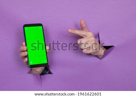 phone with green screen in hand on purple background, hand gesture, through the background hand slot