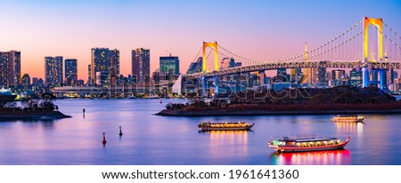 Aerial Panorama Skyline of Rainbow Bridge and Symbolic Tokyo Tower with Twilight Sky at Blue Hour in the evening with a few lighten boats in the river.