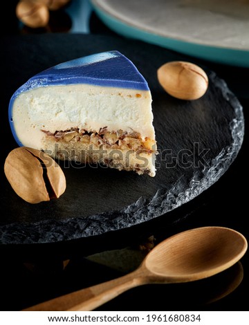 Delicate mousse cake covered with blue icing with a leopard pattern with ground pecans on a dark stone background handmade