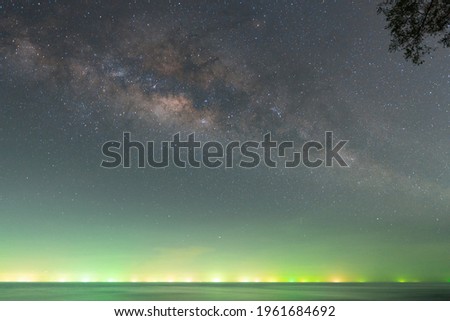 The milky way over the ocean in the night with green light from squid catching boat in the middle of the sea. This picture have noise or grain from long exposure.