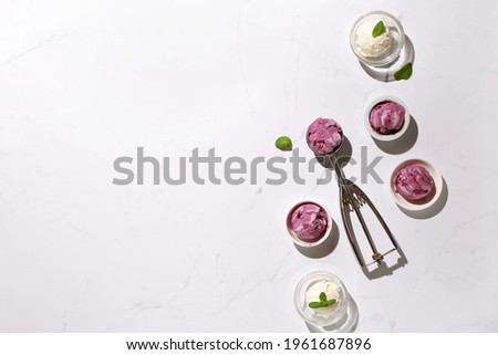 Homemade yogurt vanilla blueberry ice cream and fresh mint on natural stone marble background. Healthy low calorie summer dessert food concept. Top view, copy space. Hard sun shadows.