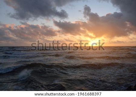 Baltic sea shore under a blue sky with glowing pink and golden sunset clouds after the storm. Crashing waves. Nature, environmental conservation, ecotourism. Picturesque panoramic scenery