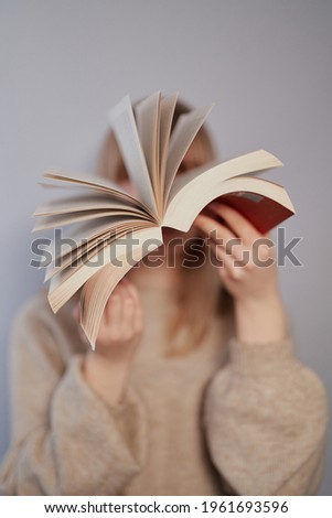 Knowledge, homeschooling or educational concept. Young blonde university or college student girl dressed in beige sweater happy leafing through a book on a gray background. High quality vertical photo