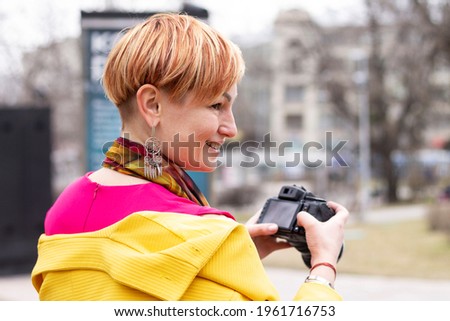 A girl photographer in a yellow coat with a camera in a city park. Close-up