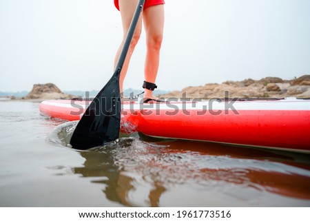 Stand up paddleboarding women paddle on the beach Happily on a paddleboard on the red water. Close up picture Young model legs on the beach during the summer vacation