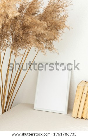 Home decor mock-up, blank picture frame near white painted concrete wall , dry Cane Reeds and old books