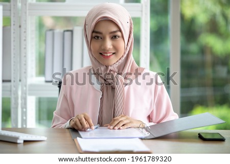 Happy Muslim business woman in traditional clothing smiling and working in office
