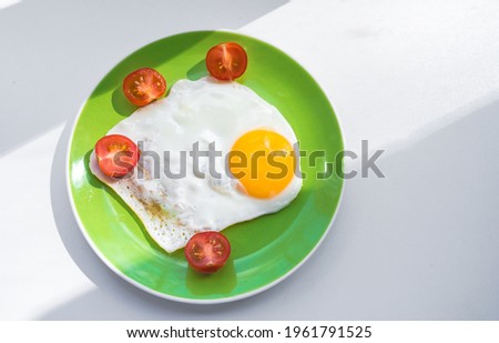 A freshly cooked hot fried egg and cherry tomatoes cut in half lie on a green plate. Healthy breakfast. Close-up. View from above.