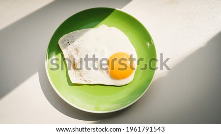A freshly cooked hot fried egg sits on a green plate. Healthy breakfast. Close-up. View from above.