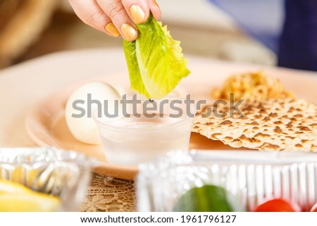 A woman's hand at the Easter Seder table dips maror and karpas in salt water. Horizontal photo