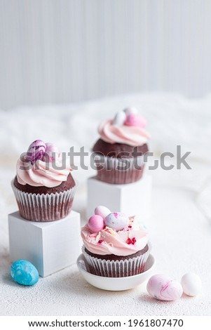 Three Easter chocolate cupcakes with caramel filling and decoration of small Easter eggs from marzipan on the white background. Selective focus