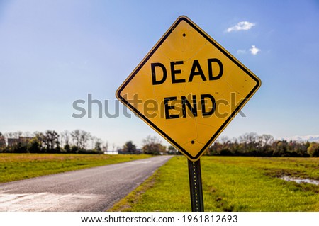 Dead End road sign with a road going to horizon in the background. Versatile image for bussiness or project failure, road blocks, problems concepts with copy space. Sunny day behind.