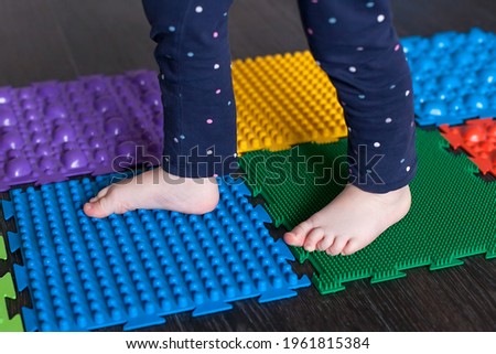 The legs of a small child on orthopedic mats. Bright surfaces for walking and forming the correct arch of the foot. Massage puzzle mat.