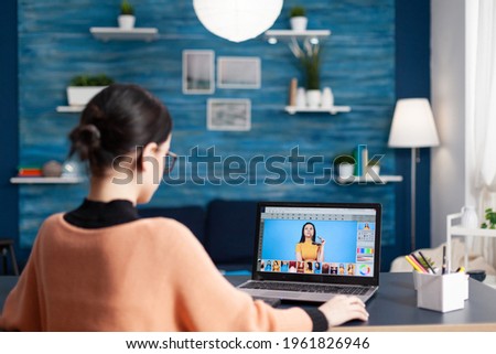 Creative photographer student editing pictures while changing color grade, retouching photos using laptop computer. Young editor sitting at desk table in living room studying photography design