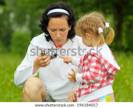 Mom and daughter together take pictures. Mom teaches young daughter photographing outdoors.