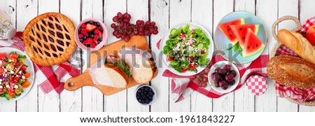 Summer picnic food table scene. Selection of cold salads, sandwiches, fruit and treats. Top view over a white wood banner background.
