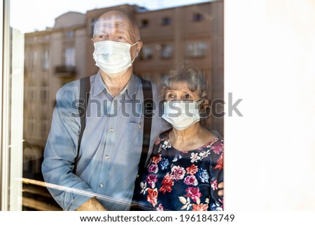 Worried senior couple looking through window at home during coronavirus COVID-19 epidemic