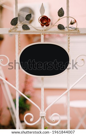 Empty oval sign on the background of a beautiful forged white fence with flowers