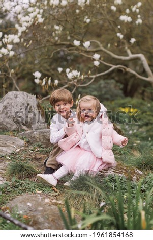 Happy children having fun in the park. Sitting. Little girl and boy playing together outdoors. Magnolia flowering.