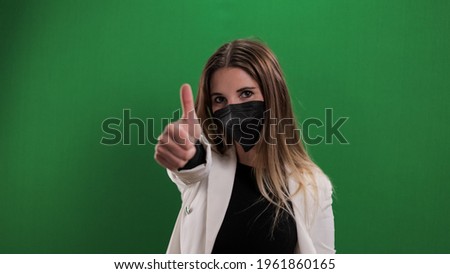 Young woman wearing face mask makes thumbs up gesture - studio photography